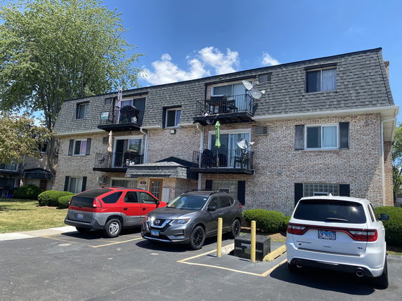 Front view of a three-story apartment building with balconies and parking space in front.