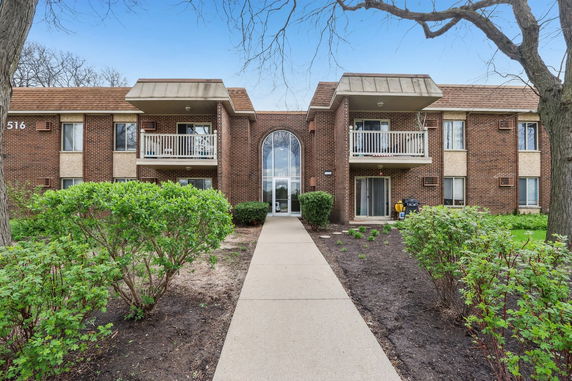 Front view of a brick apartment building with balconies and an arched entrance.