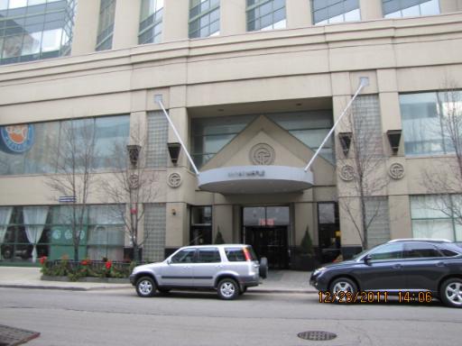 Front view of a multi-story building with wide glass windows and cars parked in front.