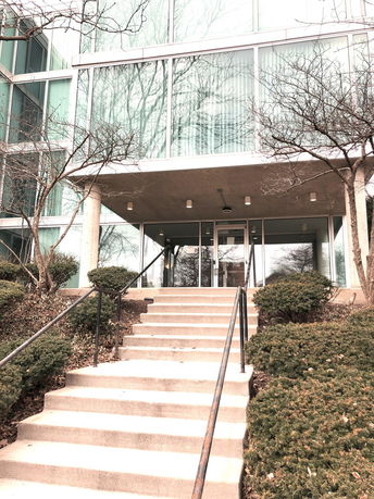 Front view of a modern glass building with stairs leading to the entrance.