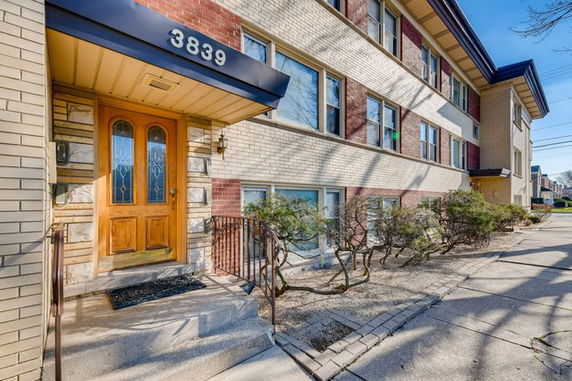 Front view of a multi-story building with brick facade and a wooden entrance door.