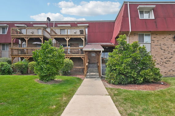 Front view of a multi-story building with red roofing and wooden balconies.
