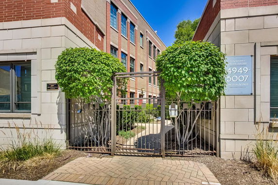 Front view of a multi-story brick building with gated entrance and surrounding landscaping.