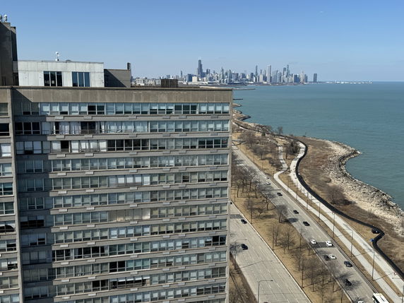 Panoramic view of a tall building by a lake with a city skyline in the background.