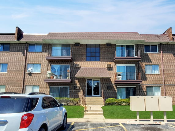 Front view of a three-story brick apartment building with balconies.
