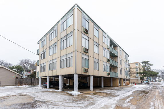 Front view of a multi-story apartment building on stilts with parking space beneath.