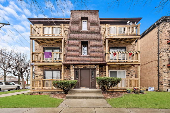 Front view of a multi-story brick building with balconies and a unique central roof design.