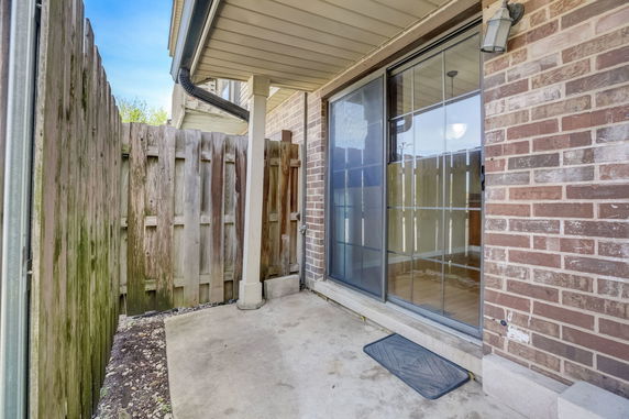 View of a partially covered patio area with brick wall and sliding glass door.