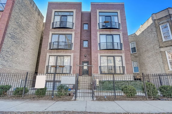 Front view of a three-story brick apartment building with balconies.