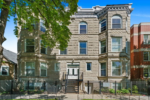 Front view of a multi-story residential building with large windows and a gated entrance.