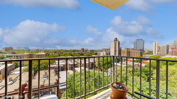 Panoramic view from a balcony overlooking a cityscape with numerous buildings and greenery.
