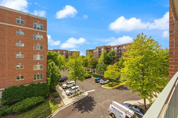 View of multiple brick apartment buildings and a parking lot with trees lining the area.