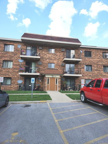 Front view of a three-story brick apartment building with balconies.