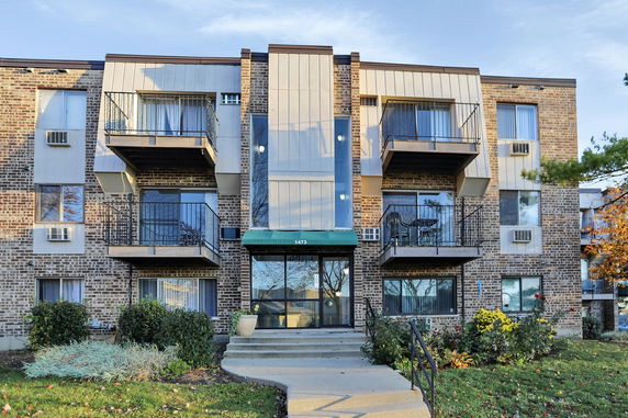 Front view of a three-story brick apartment building with balconies.
