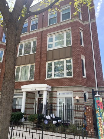 Front view of a multi-story brick building with large windows and an entrance with white columns.