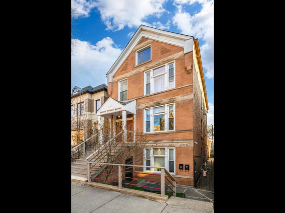 Front view of a multi-story brick house with a wooden porch and staircase.