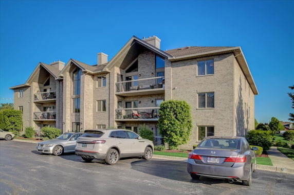 Front view of a multi-story residential building with balconies and parking area.