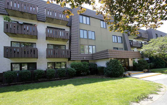 Front view of a multi-story apartment building with balconies and a tiled roof.