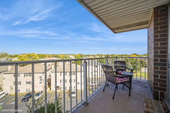 Balcony with patio chairs overlooking residential buildings and parking area.