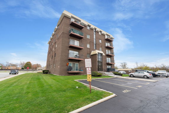 Front view of a multi-story brick apartment building with balconies and a parking area.