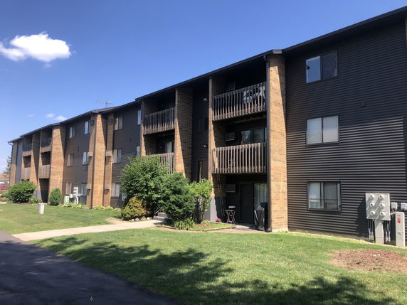 Front view of a multi-story apartment building with balconies and brick exterior.