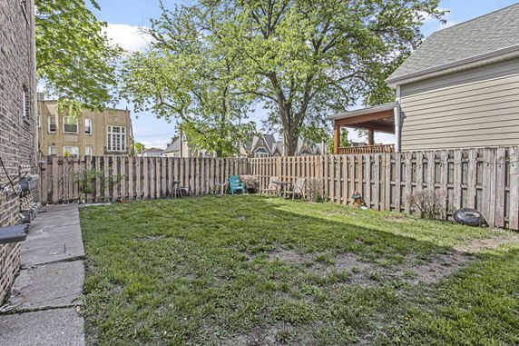 Backyard view with grass, wooden fence, and trees.