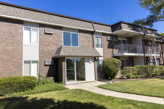 Front view of a multi-story brick apartment building with balconies and a glass entrance.