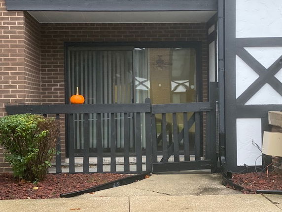 Front view of a building with a black railing and a pumpkin on it, featuring a brick wall and a glass sliding door.
