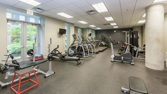 Interior view of a gym with exercise equipment including treadmills, ellipticals, and weightlifting benches.