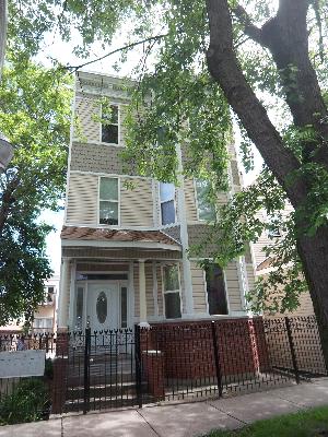 Front view of a three-story house with a brick fence and a decorative front door.
