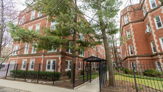 Front view of a multi-story brick apartment building with a gated entrance.
