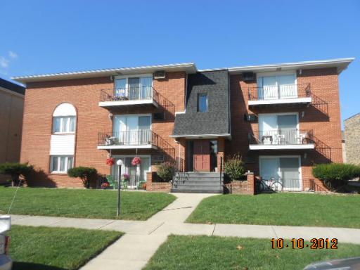 Front view of a three-story brick apartment building with balconies.