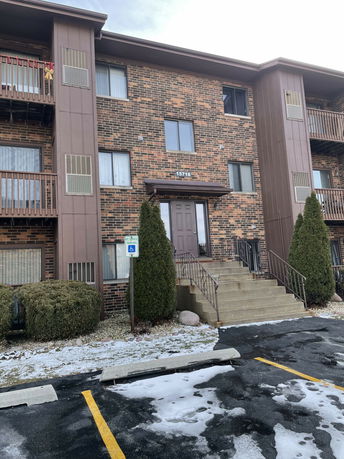 Front view of a multi-story brick apartment building with stairs leading to the entrance.