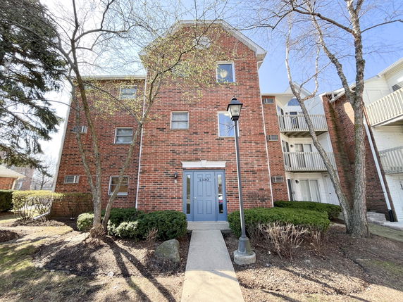 Front view of a multi-story brick building with trees and a pathway leading to the entrance.