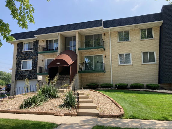 Front view of a two-story apartment building with a central entrance canopy and surrounding landscaping.