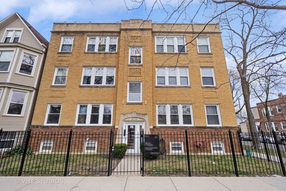 Front view of a three-story brick apartment building with multiple windows and a gated entrance.