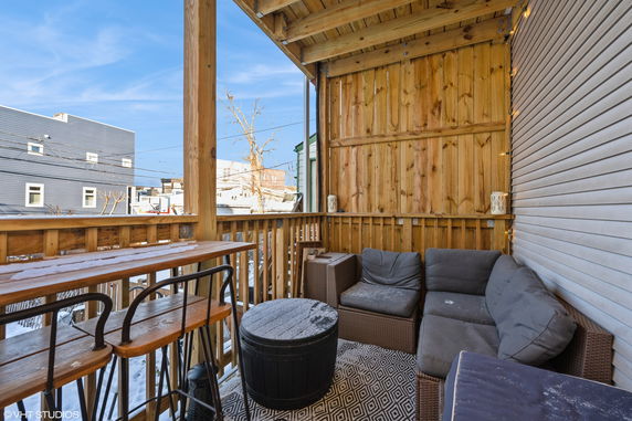 Rooftop with wooden furniture and cushions under a pergola-style cover.