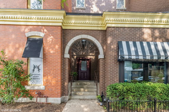 Front view of a two-story brick building with an arched entrance and windows with awnings.