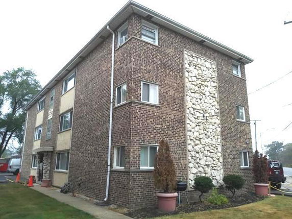Front and side view of a three-story brick apartment building with decorative stone element.