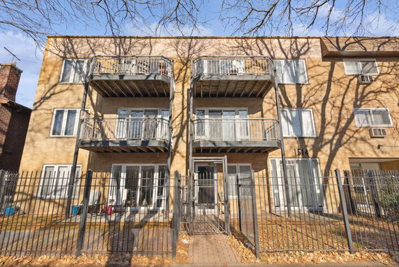 Front view of a three-story building with balconies and a fenced entrance.