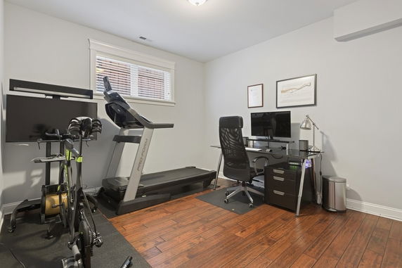 Indoor fitness room with exercise equipment and a desk.
