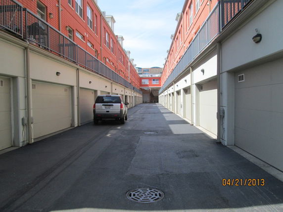 Outdoor parking area in between rows of buildings with garages.