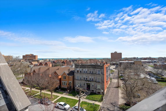 Panoramic view of a neighborhood with houses, apartment buildings, and distant water body under a blue sky.