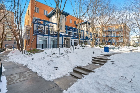 Front view of a multi-story building with a modern design and balconies, surrounded by snow-covered ground.