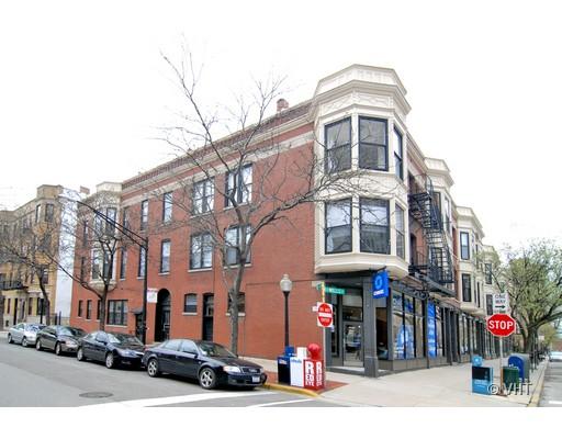 Street view of a multi-story brick building with bay windows and a ground-level storefront.