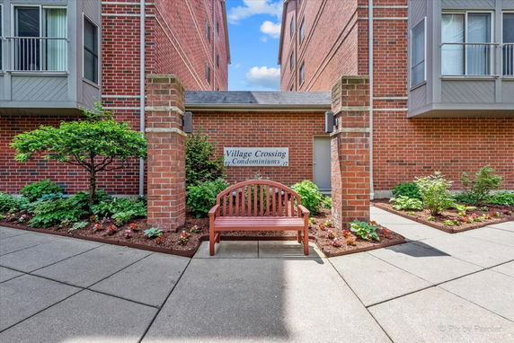 Front view of a condominium building with brick exterior and a wooden bench.