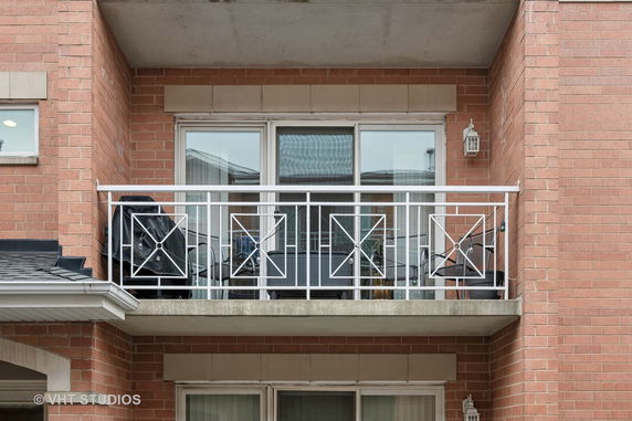 Front view of a brick building with a balcony featuring white metal railings and glass doors.