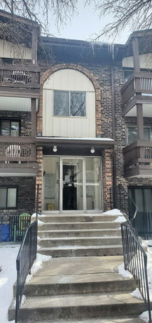 Front view of a multi-story brick apartment building with balconies and an entrance with stairs.