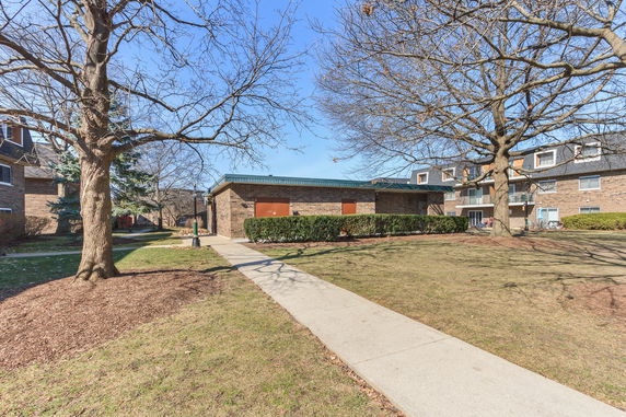 Front view of two-story brick apartment buildings with a walkway and trees in the foreground.