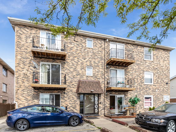 Front view of a three-story brick apartment building with balconies.